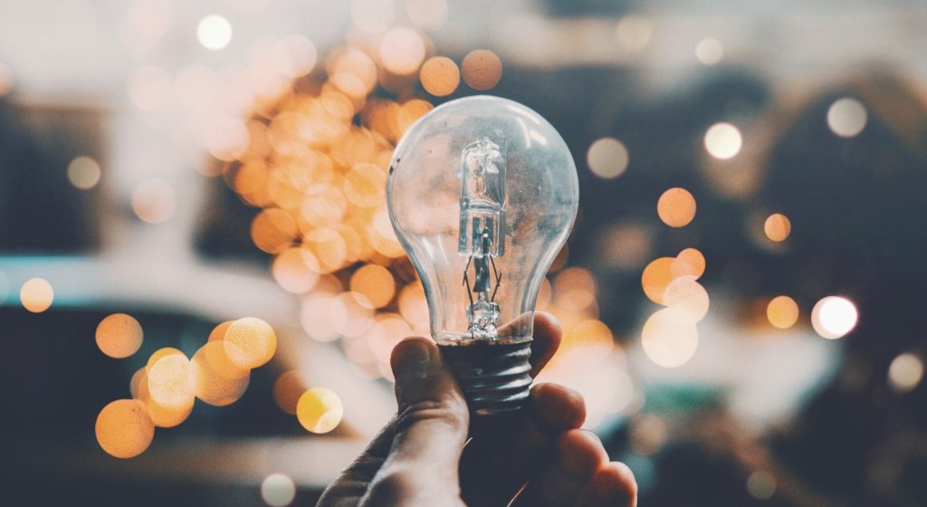 Glühbirne wird vor orangenen Lichtreflexionen in der Hand gehalten.