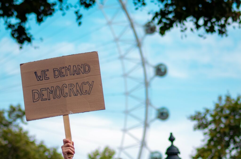 Ein Protestschild, auf dem "We demand democracy" steht, wird hochgehalten.