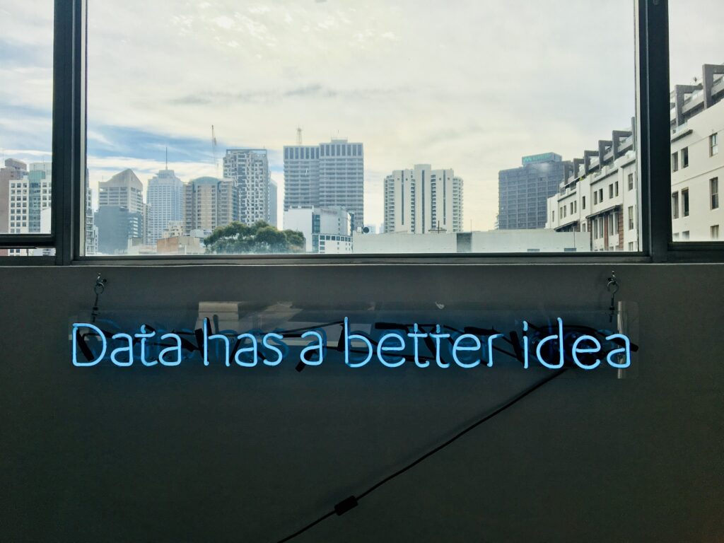 Unter einem Fenster, das die Skyline einer Großstadt zeigt, steht in blauen Leuchtbuchstaben "Data has a better idea".