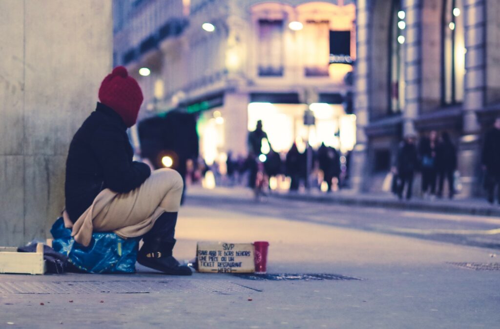 Foto eines Obdachlosen, der auf einer Einkaufsstrasse auf dem Boden sitzt.