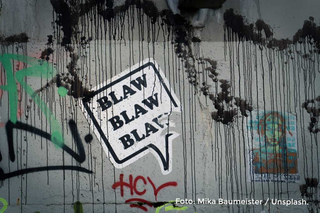Symbolbild für Hate Speech im Internet. Foto einer Wand mit Graffiti, auf der ein Sprechblasensticker klebt.