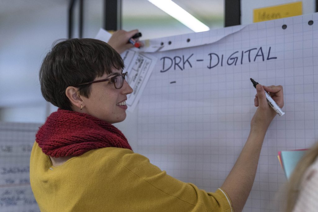 Jennifer Geiser vom DRK steht bei einem Innovation-Workshop vor einem Flipchart und schreibt "DRK-Digital" als Überschrift darauf.